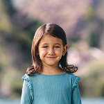 A young girl with shoulder-length brown hair wearing a green t-shirt, smiling